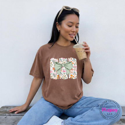 Espresso brown tee with a sage green bow over watercolor wildflower panels