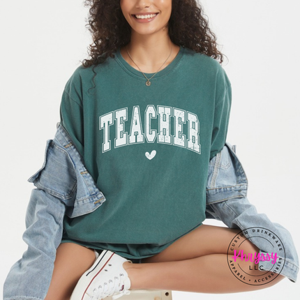 Woman in a Blue Spruce tee with a distressed Teacher varsity arch and heart.