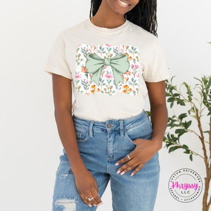 Ivory tee with a sage green bow over watercolor wildflower panels