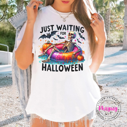 White tee featuring a skeleton lounging on a pool float with bats and pumpkins