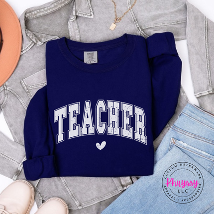 Flat lay of a True Navy teacher varsity long sleeve tee with a heart graphic.