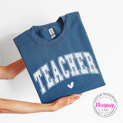 Folded Indigo Blue crewneck sweatshirt with distressed Teacher varsity lettering and heart.