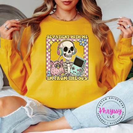 Gold crewneck sweatshirt showing a laid-back skeleton in front of a striped retro sunset.