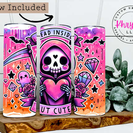 Colorful tumbler with a pink and orange design, featuring a skull holding a heart, on a wooden surface with a plant in the background.