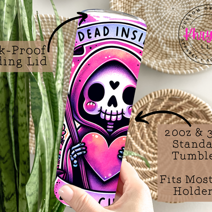 Tumbler with pink skull design and text, held by a hand, with decorative elements in the background.