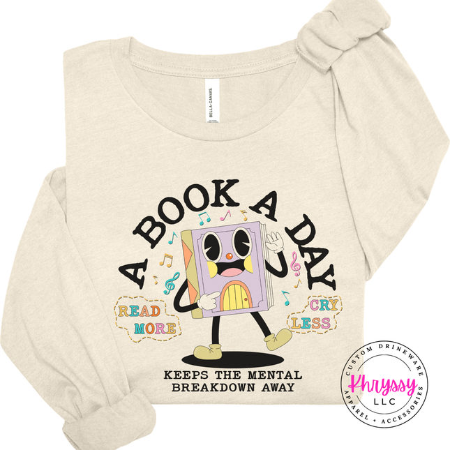 Heather Natural Bella Canvas long sleeve printed with the retro cartoon A Book A Day Keeps The Mental Breakdown Away graphic.