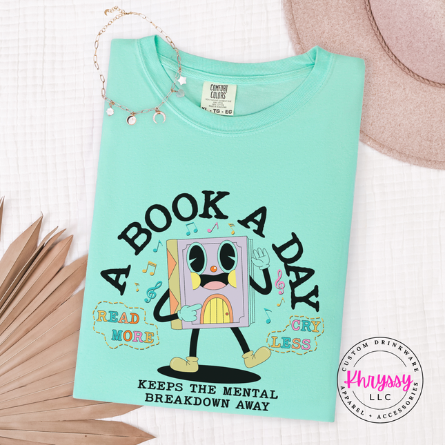 Island Reef soft cotton tee featuring the pastel lavender book character and A Book A Day lettering.