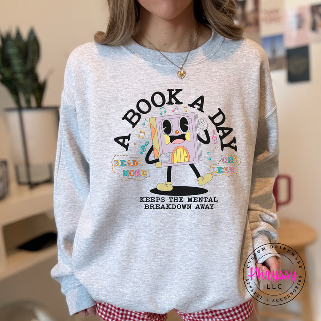 Ash Grey Gildan crewneck with retro cartoon book character A Book A Day Keeps The Mental Breakdown Away print.