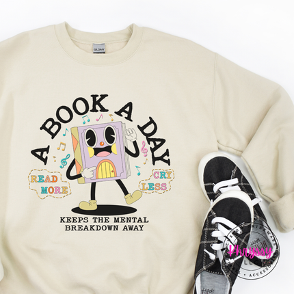 Sand Gildan crewneck showing the multicolor retro book character and mental breakdown away text.