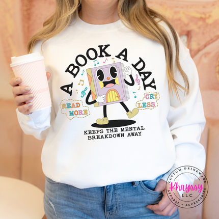 White Gildan crewneck with the retro cartoon book character A Book A Day mental breakdown away print.