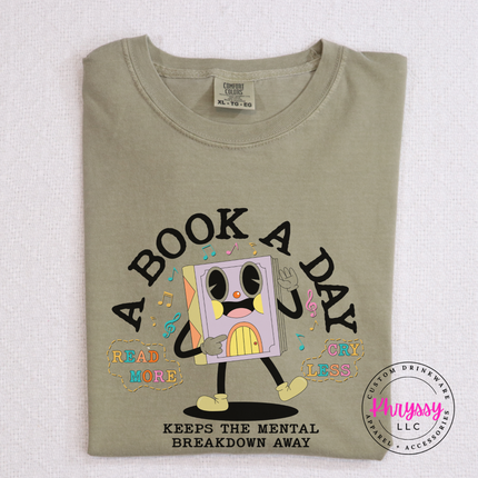 Khaki tee showing the multicolor retro book character with read more cry less text.