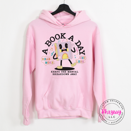Light pink Gildan hoodie with the retro cartoon book character A Book A Day mental breakdown away print.