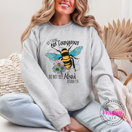 Person wearing a gray sweatshirt with a bee design and text, sitting on a couch.