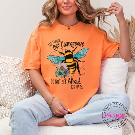 Person wearing an orange t-shirt with a bee graphic and text, sitting on a couch.