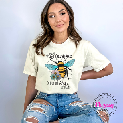 Woman wearing a white t-shirt with a bee graphic and text, sitting against a light gray background.