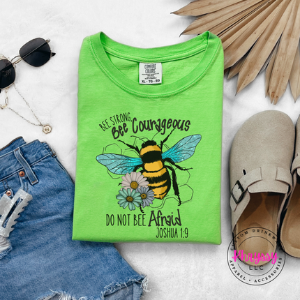 Green t-shirt with bee graphic and text on a white surface with accessories.