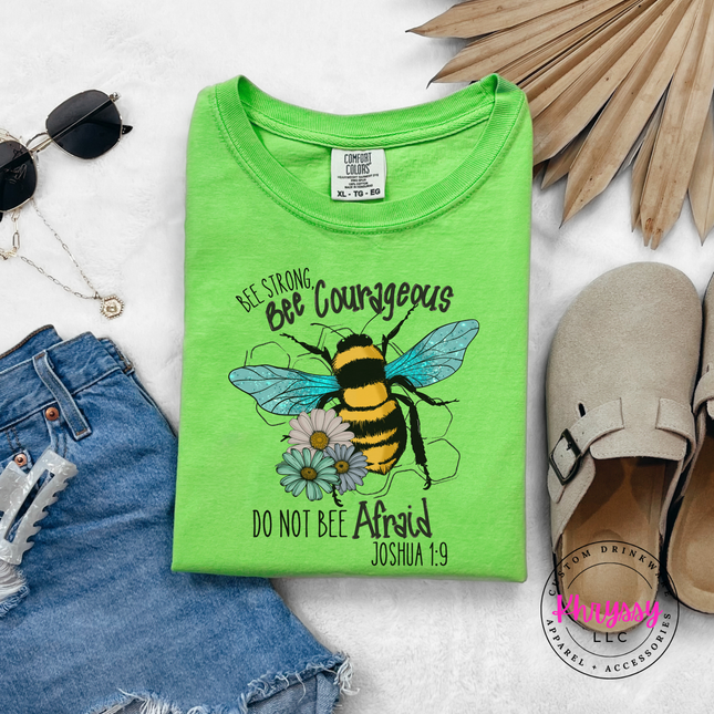 Green t-shirt with bee graphic and text on a white surface with accessories.