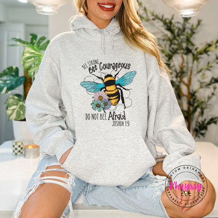 Person wearing a gray hoodie with a bee graphic and text, sitting indoors.