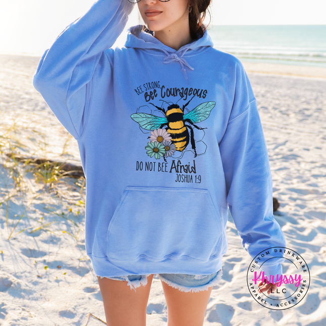 Person wearing a blue hoodie with a bee design on a sandy beach