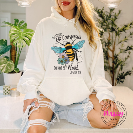 Person wearing a white hoodie with a bee design and text, sitting in a room with plants.