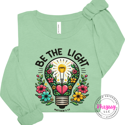 Mint long sleeve tee with bold Be The Light lettering above a floral bulb