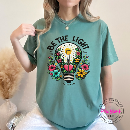 Light Green tee with bold Be The Light lettering above a floral bulb
