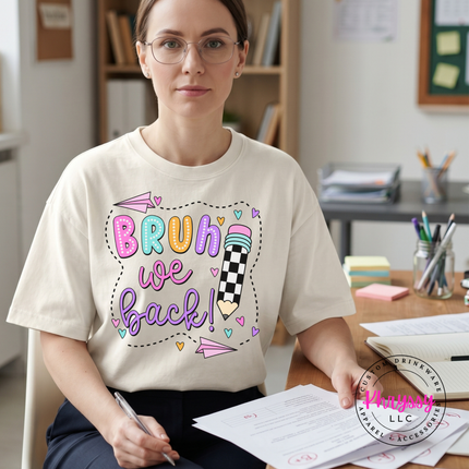 Ivory teacher tee featuring colorful Bruh We Back lettering and paper airplanes.
