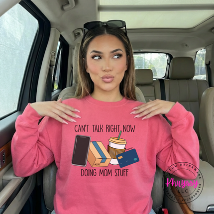 Woman wearing a Safety Pink crewneck sweatshirt with the doing mom stuff design