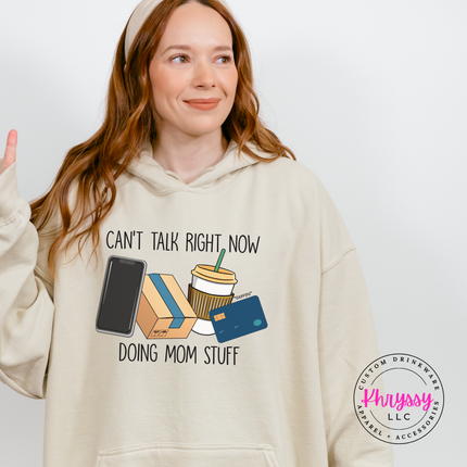 Sand hoodie showing the doing mom stuff graphic with coffee and a phone