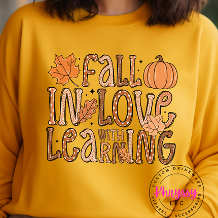 A person wearing a yellow unisex sweatshirt with the text 'FALL IN LOVE WITH LEARNING' and decorative elements such as leaves and a pumpkin.