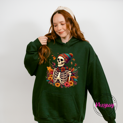 Forest colored hoodie featuring a scarf-wearing skeleton among autumn florals.