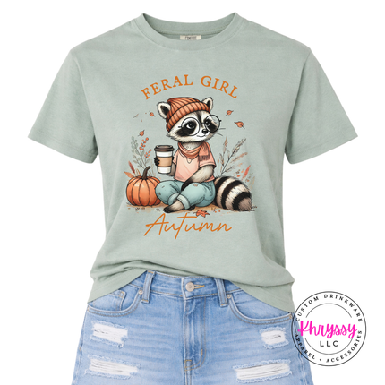 Bay colored tee featuring a raccoon holding coffee beside a pumpkin.