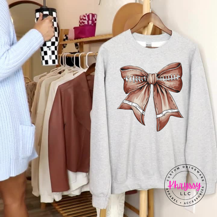 Ash heavyweight crewneck with a brown football-shaped lace bow graphic.