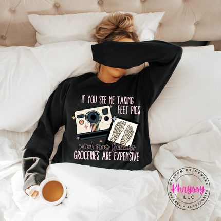 Person wearing a black sweatshirt with a humorous design, lying on a bed with a cup of coffee.
