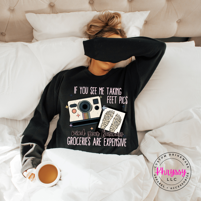 Person wearing a black sweatshirt with a humorous design, lying on a bed with a cup of coffee.