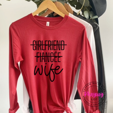 Red long-sleeve shirt with 'Girlfriend Fiancée Wife' text on a hanger.
