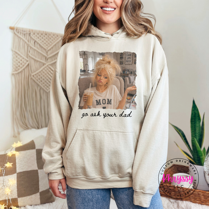 Person wearing a beige hoodie with a graphic design and text, standing in a cozy room.