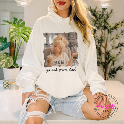 Person wearing a white hoodie with a graphic design and text, sitting in a room with plants.