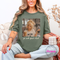 Woman wearing a green t-shirt with a graphic and text, sitting on a couch.