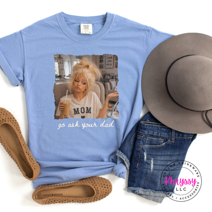 Blue t-shirt with a graphic of a person in a car, text 'go ask your dad', accompanied by a hat, sandals, and jeans on a white background.