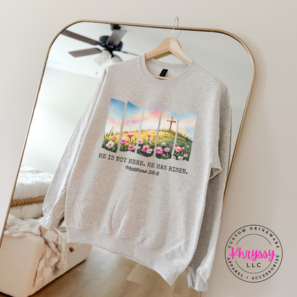 Ash crewneck sweatshirt with a He Has Risen watercolor cross and wildflowers graphic.