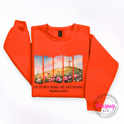 Orange crewneck sweatshirt with a watercolor Easter He Has Risen graphic and verse.