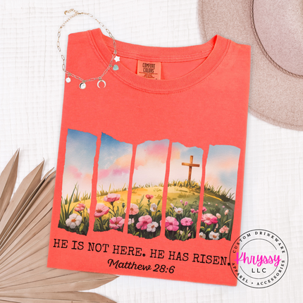 Bright Salmon garment-dyed tee with a He Has Risen watercolor cross and wildflowers graphic.