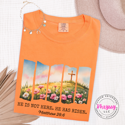 Melon garment-dyed tee with a watercolor Easter He Has Risen graphic and verse.