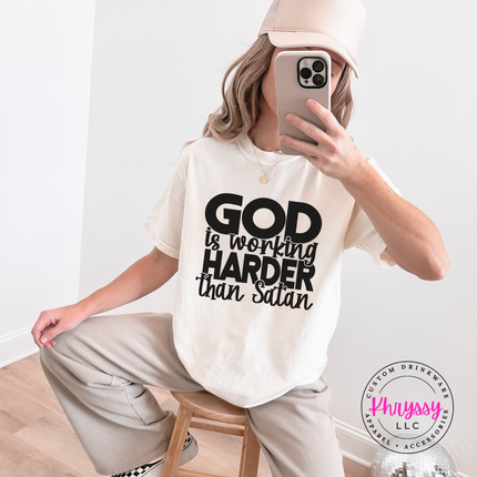 Ivory tee with an all-caps God Is Working Harder design centered on the chest