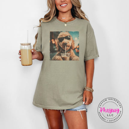 Woman wearing a khaki t-shirt with a dog graphic, holding a drink, on a white background.