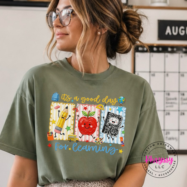 Comfort Colors teacher shirt featuring a smiling apple and dancing pencil.