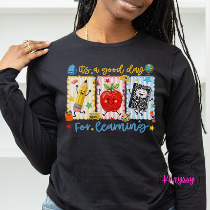 Black long sleeve tee featuring a smiling apple and school supply illustrations.
