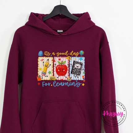 Maroon Gildan hoodie featuring a smiling apple and dancing pencil graphic.