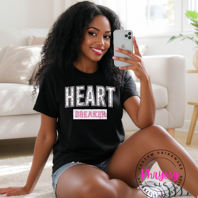 Woman wearing a black t-shirt with 'HEART BREAKER' text, sitting on the floor in a living room.
